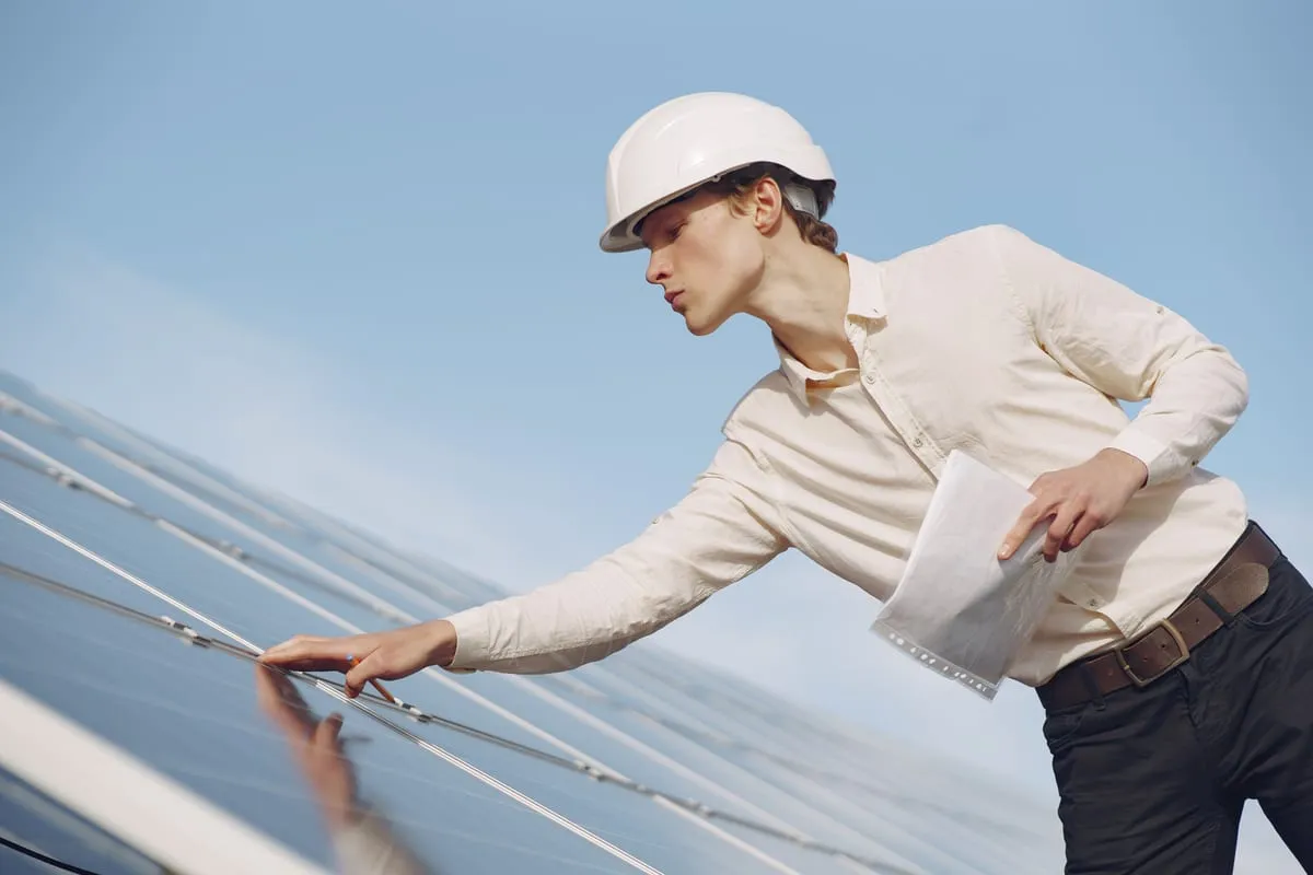 An engineer in a white hard hat inspecting a solar panel with a tablet